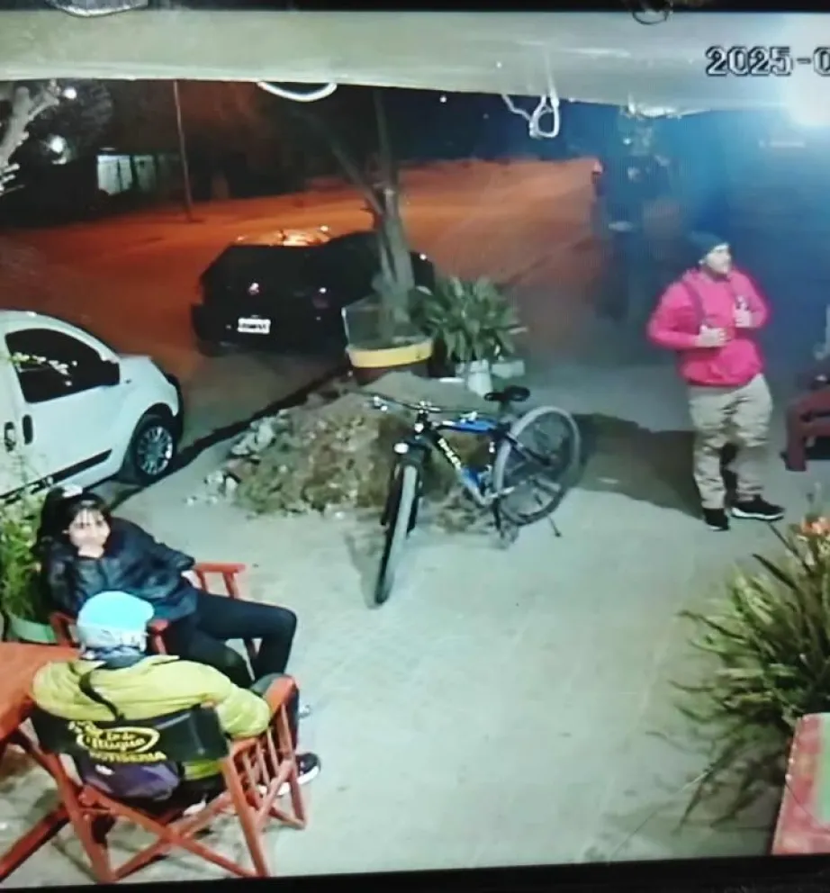 La pareja está sentada al lado de la bicicleta mientras el dueño, de rojo, espera su comida. (Foto gentileza)